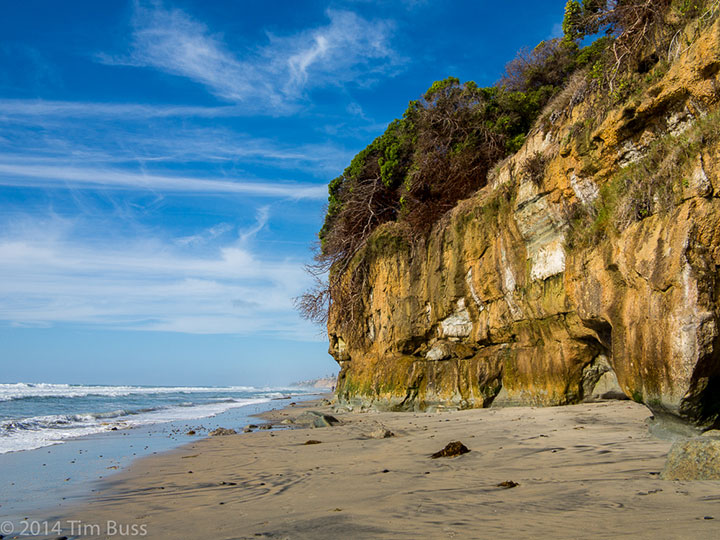 a sandy beach below a yellow cliff
